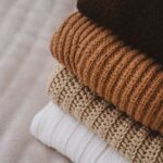 A stack of cozy, folded knitted sweaters in warm, neutral colors, perfect for autumn.