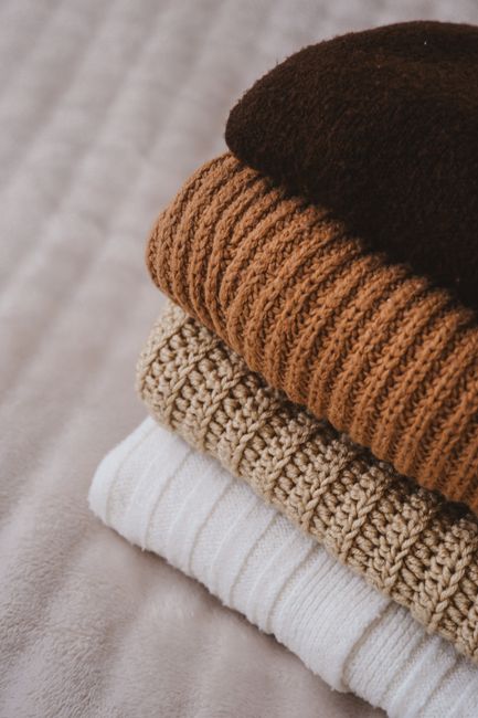 A stack of cozy, folded knitted sweaters in warm, neutral colors, perfect for autumn.