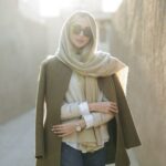 Elegant woman dressed in a coat and scarf, enjoying sunlight outdoors. A fashionable moment captured.