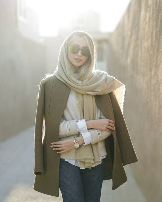 Elegant woman dressed in a coat and scarf, enjoying sunlight outdoors. A fashionable moment captured.